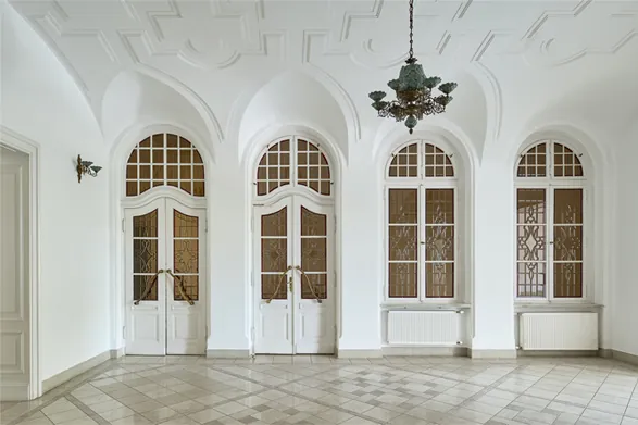 Sala z łukowymi drzwiami i oknami, żyrandolem i jasną posadzką